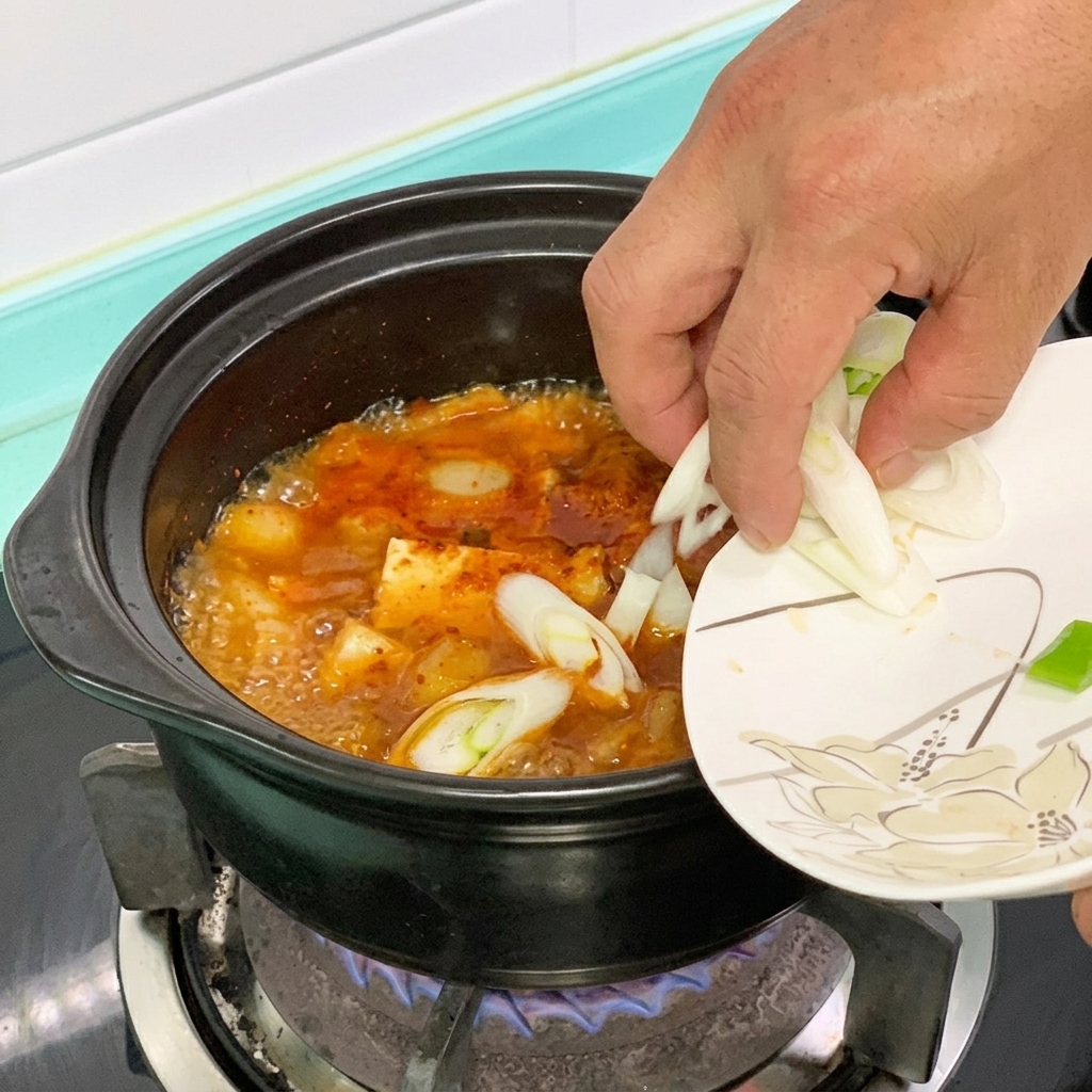 Peperoncino verde e cipollotto aggiunti in una pentola di stufato di tofu rosso.