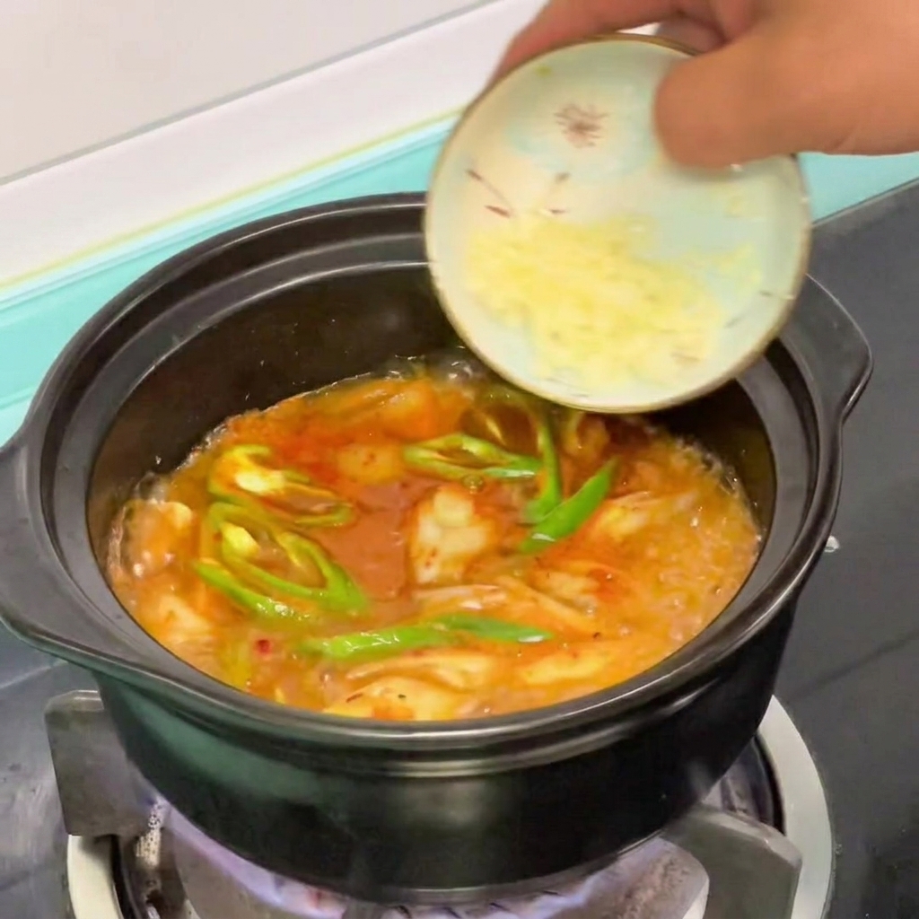 Aglio tritato aggiunto a una pentola di stufato coreano di tofu morbido in cottura.
