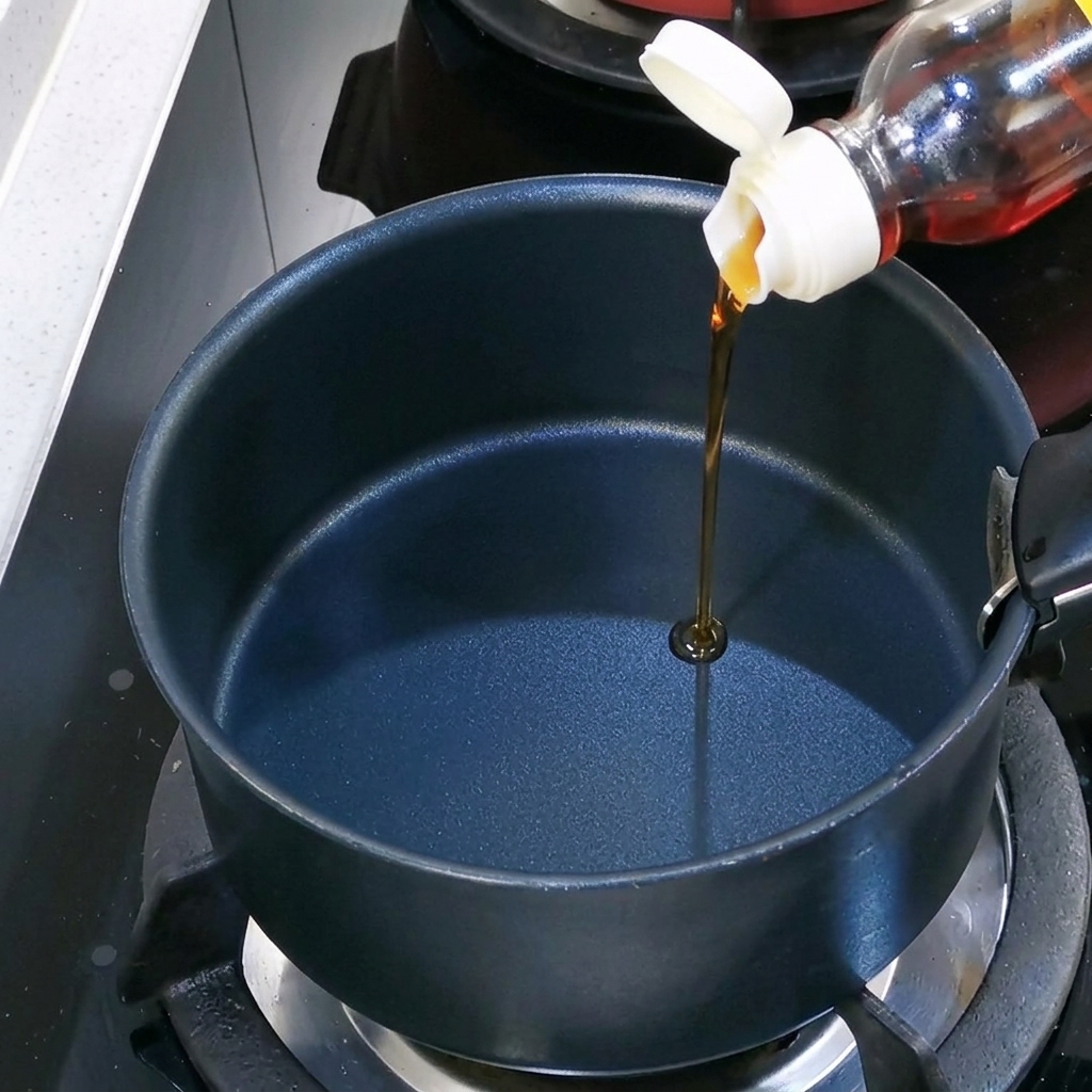 Olio di sesamo versato in una pentola nera vuota sul fornello.