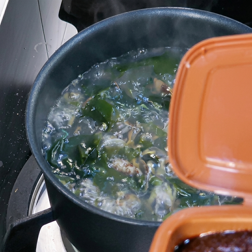 Un cucchiaio di pasta di soia coreana marrone mescolato nella zuppa bollente.