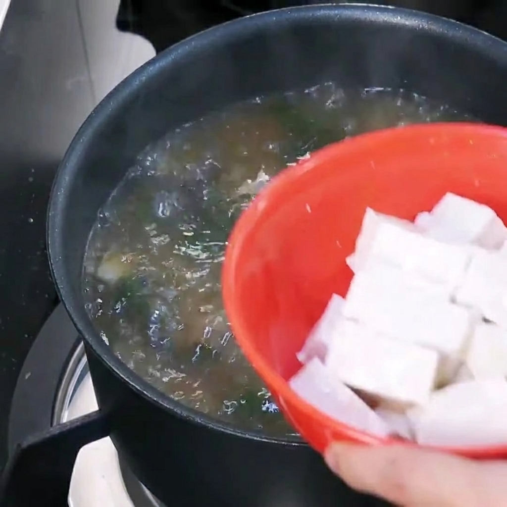 Cubetti di tofu aggiunti a una pentola di zuppa coreana di pasta di soia bollente.