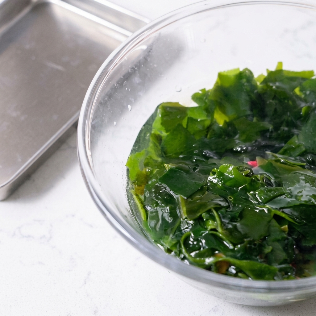 Alga wakame reidratata sollevata da una ciotola con un cucchiaio forato rosa.