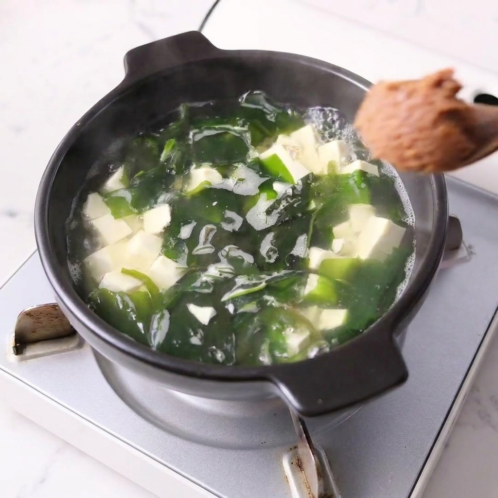 Un cucchiaio di pasta di miso mescolato nella pentola con tofu e wakame.