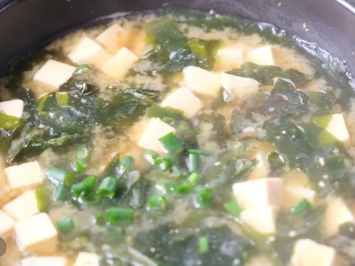 Primo piano di una pentola di zuppa di miso con tofu, alga e cipollotto fresco tritato sopra.