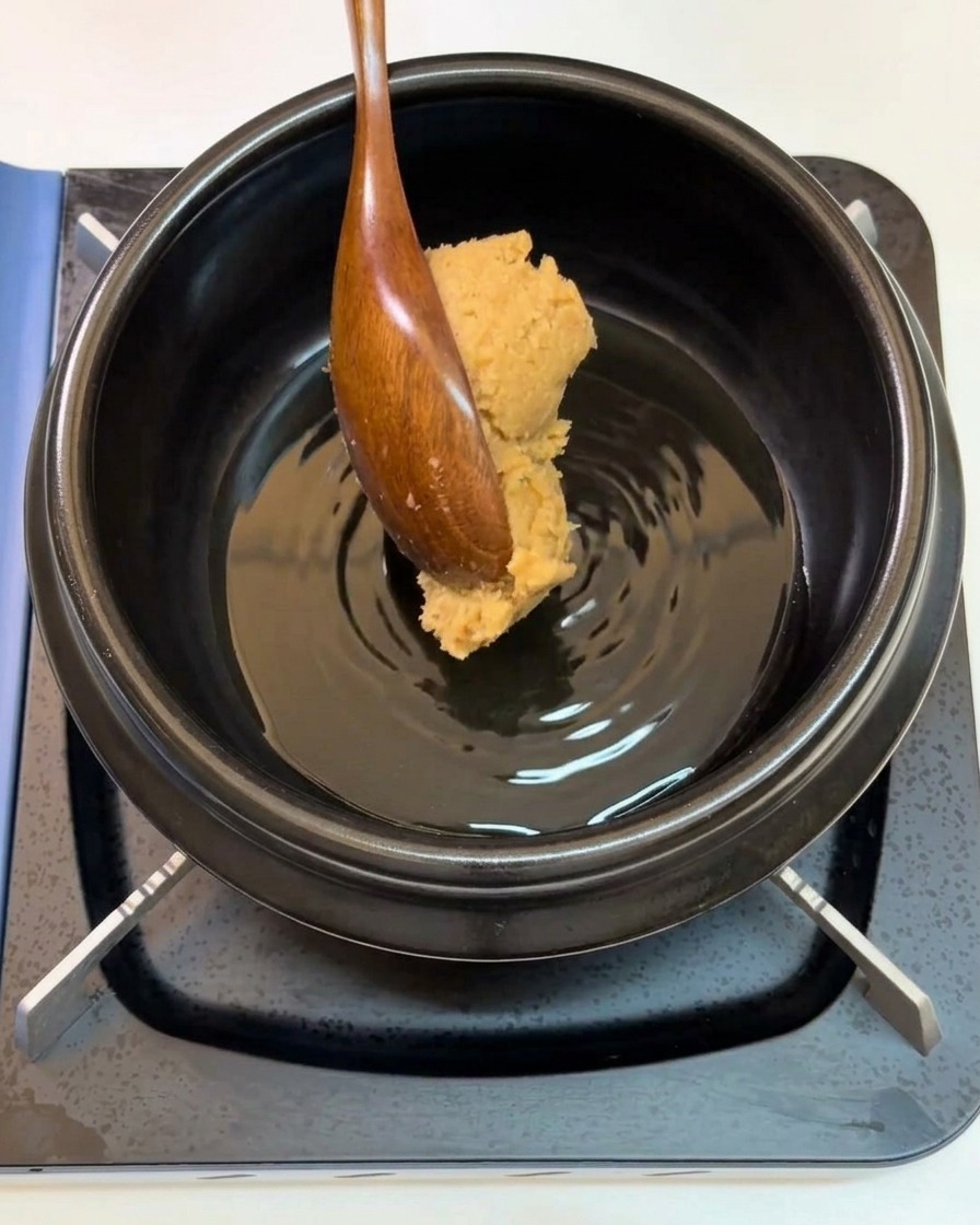 Un cucchiaio di legno aggiunge una dose di pasta di soia in una pentola.