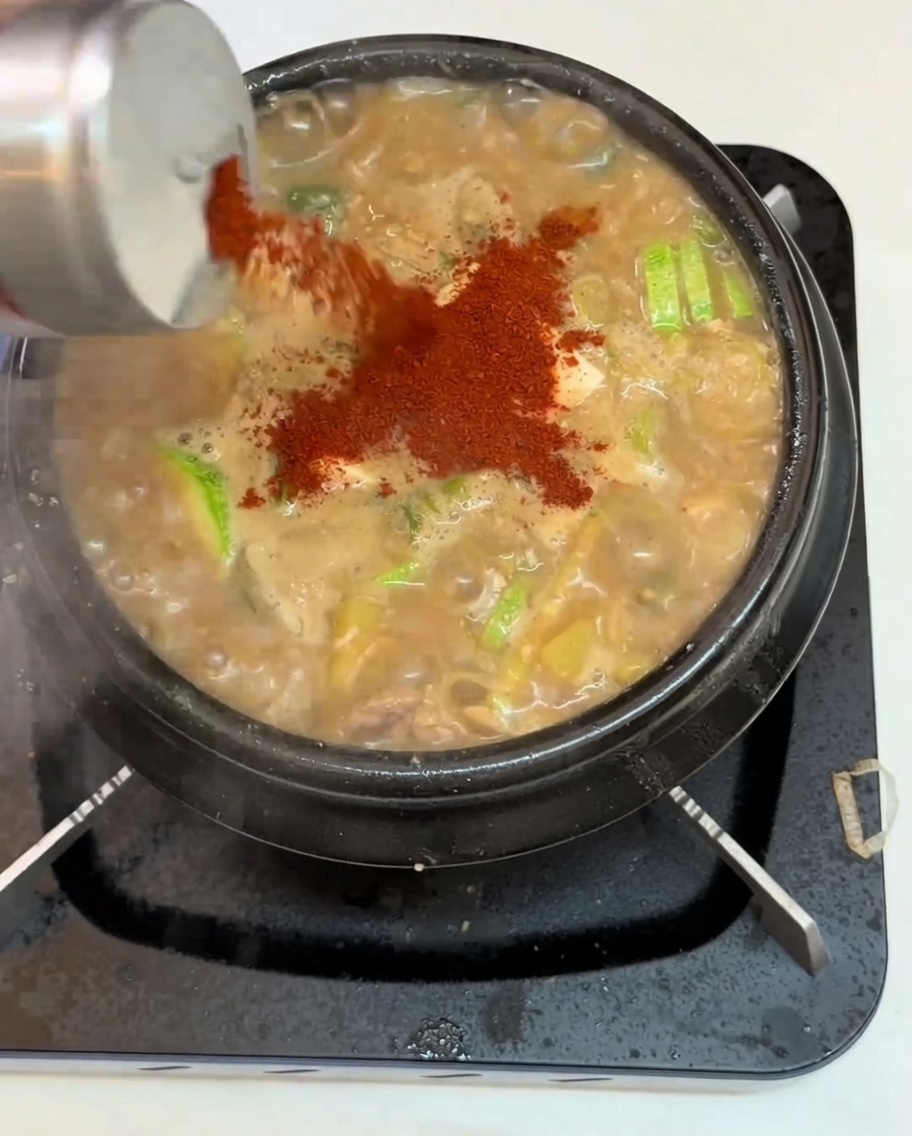Un primo piano di peperoncino in polvere versato su una pentola di stufato di pasta di soia bollente.