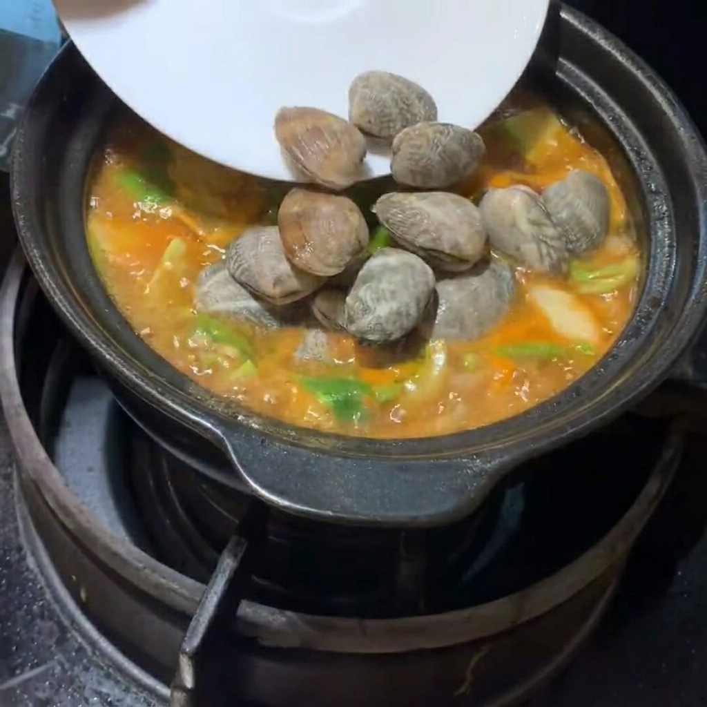 Vongole fresche e cubetti di tofu morbido delicatamente posizionati nella zuppa che bolle.