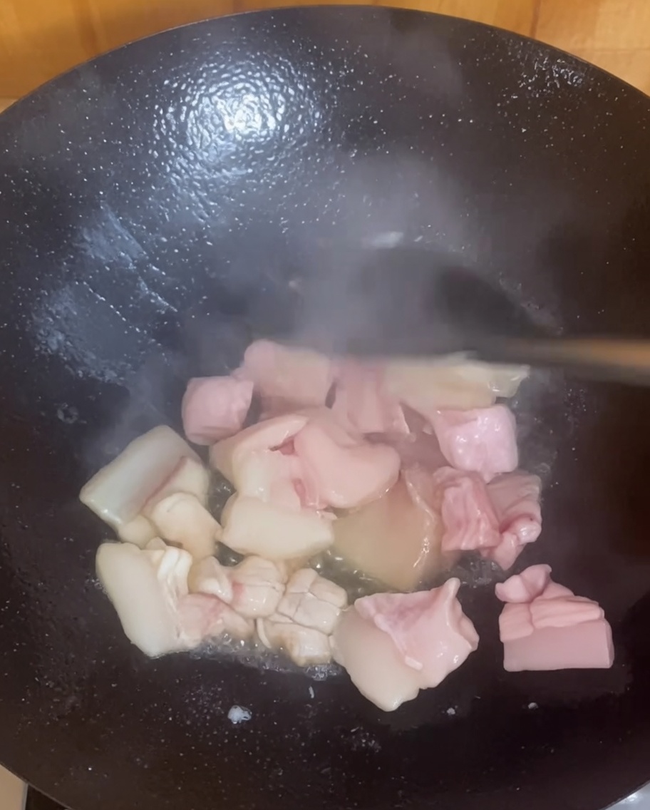 Pezzi di pancetta che sfrigolano e dorano in un wok caldo.