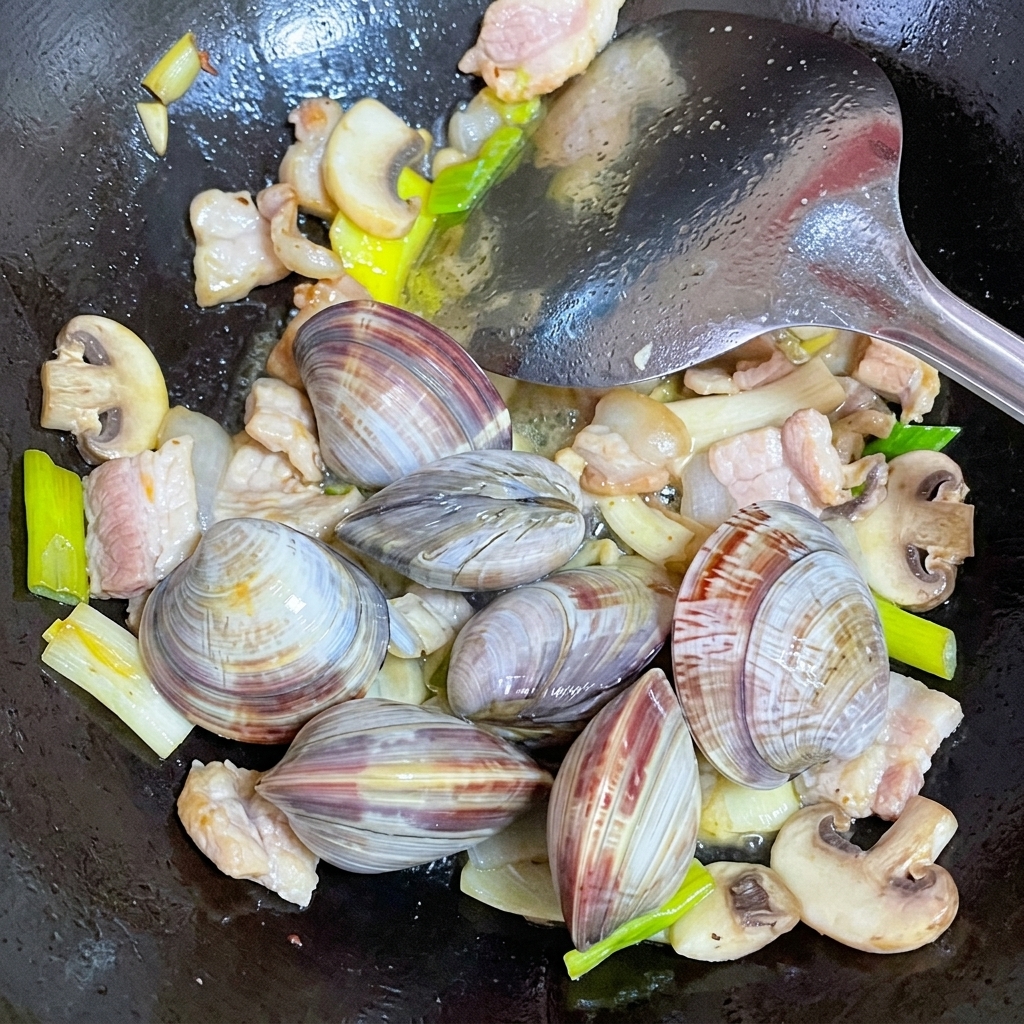 Vongole fresche pulite aggiunte in un wok con maiale e funghi.