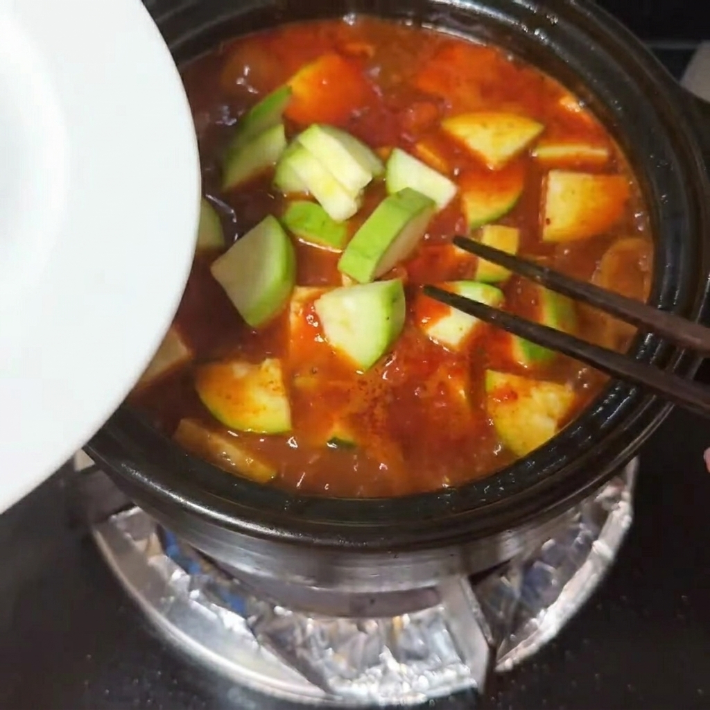 Fette di zucchina e cubetti di tofu vellutato morbido inseriti in una zuppa rossa che sobbolle.