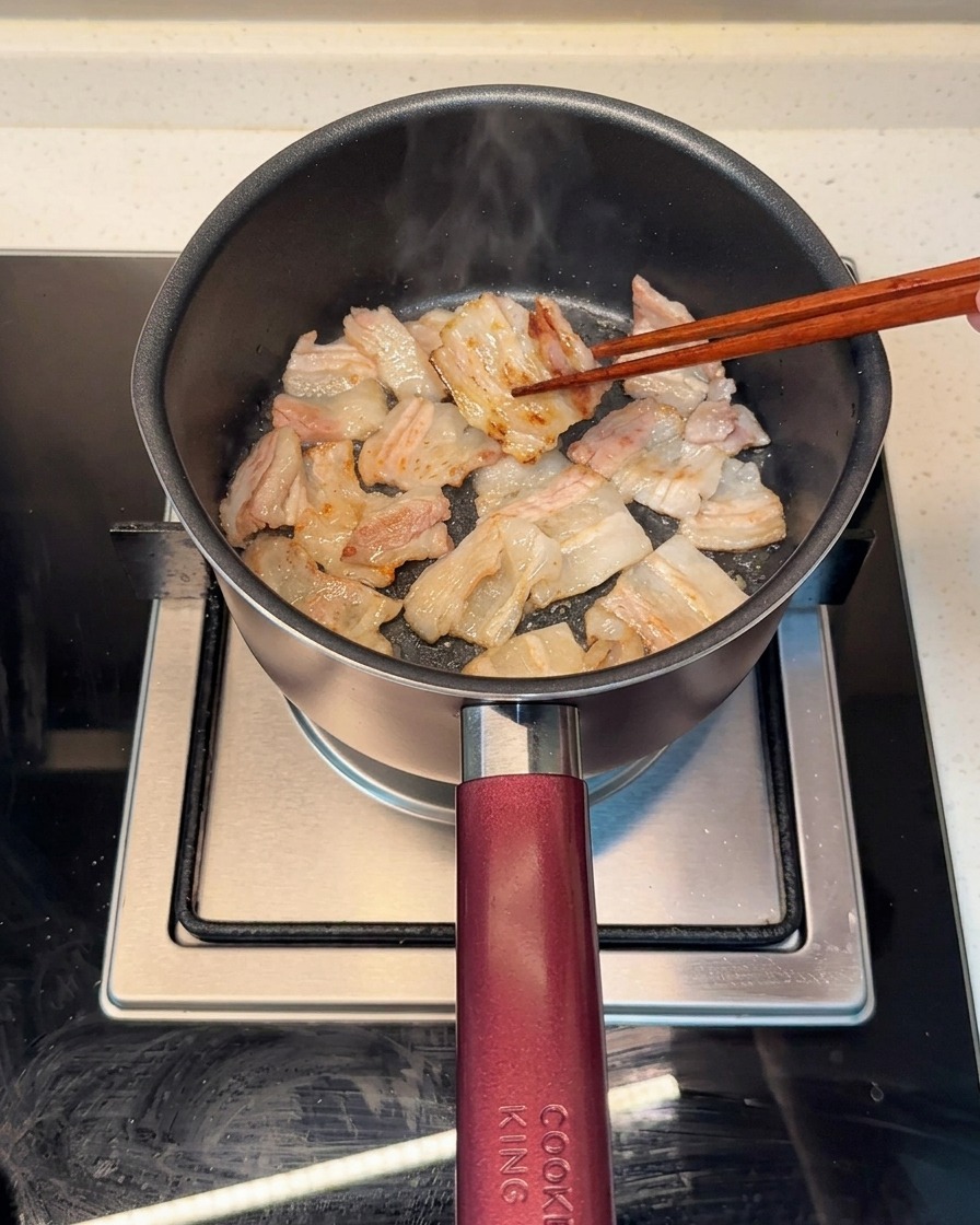 Fette di pancetta di maiale che rosolano uniformemente in una pentola calda, con il grasso che si scioglie.
