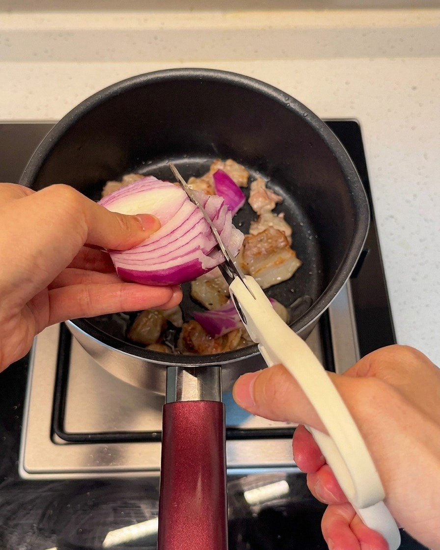 Tagliare la cipolla rossa fresca direttamente nella pentola con la pancetta usando le forbici da cucina.