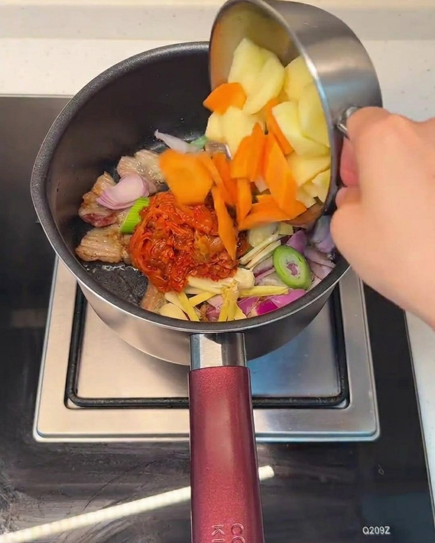 Aggiunta di carote e patate a cubetti nella pentola con il composto di carne e kimchi.