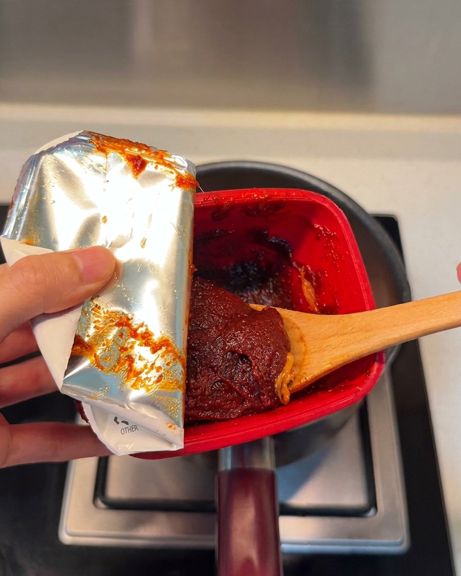Un cucchiaio di ricca pasta di peperoncino coreana rossa aggiunta nella pentola.