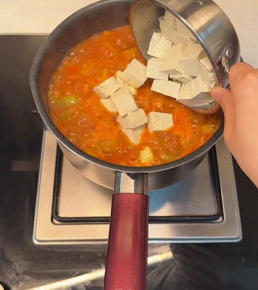 Tofu a cubetti aggiunto in una pentola di stufato piccante coreano in ebollizione.