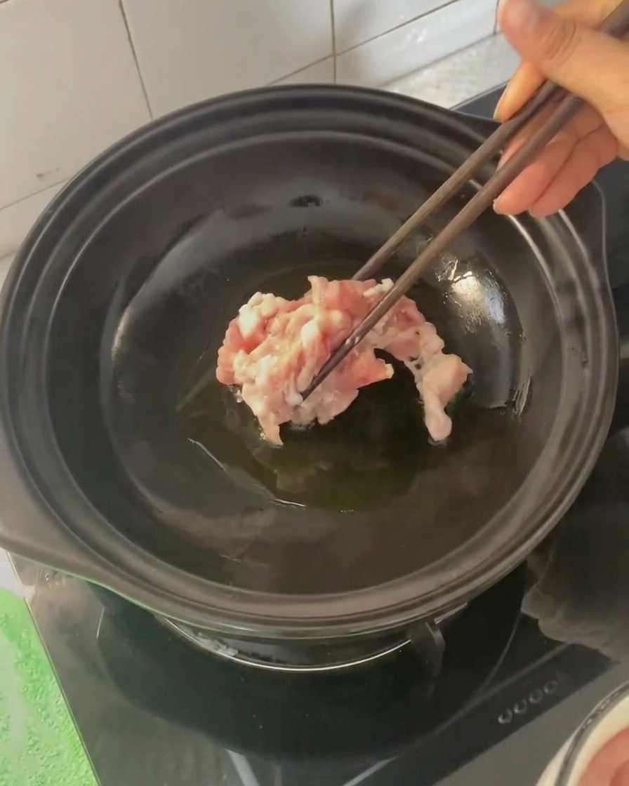 Fette di pancetta aggiunte nella pentola di coccio calda con le bacchette.