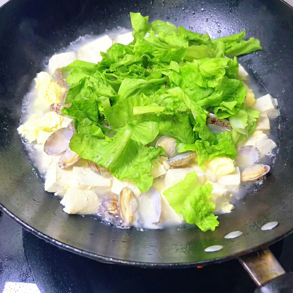 Una padella di zuppa di vongole e tofu finita che viene mescolata delicatamente con un mestolo.