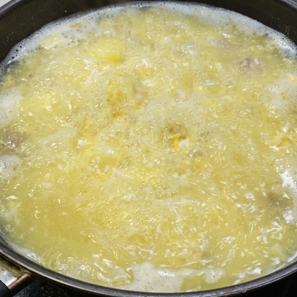 Sale e pepe bianco aggiunti alla zuppa di tofu e uova salate che sobbolle.