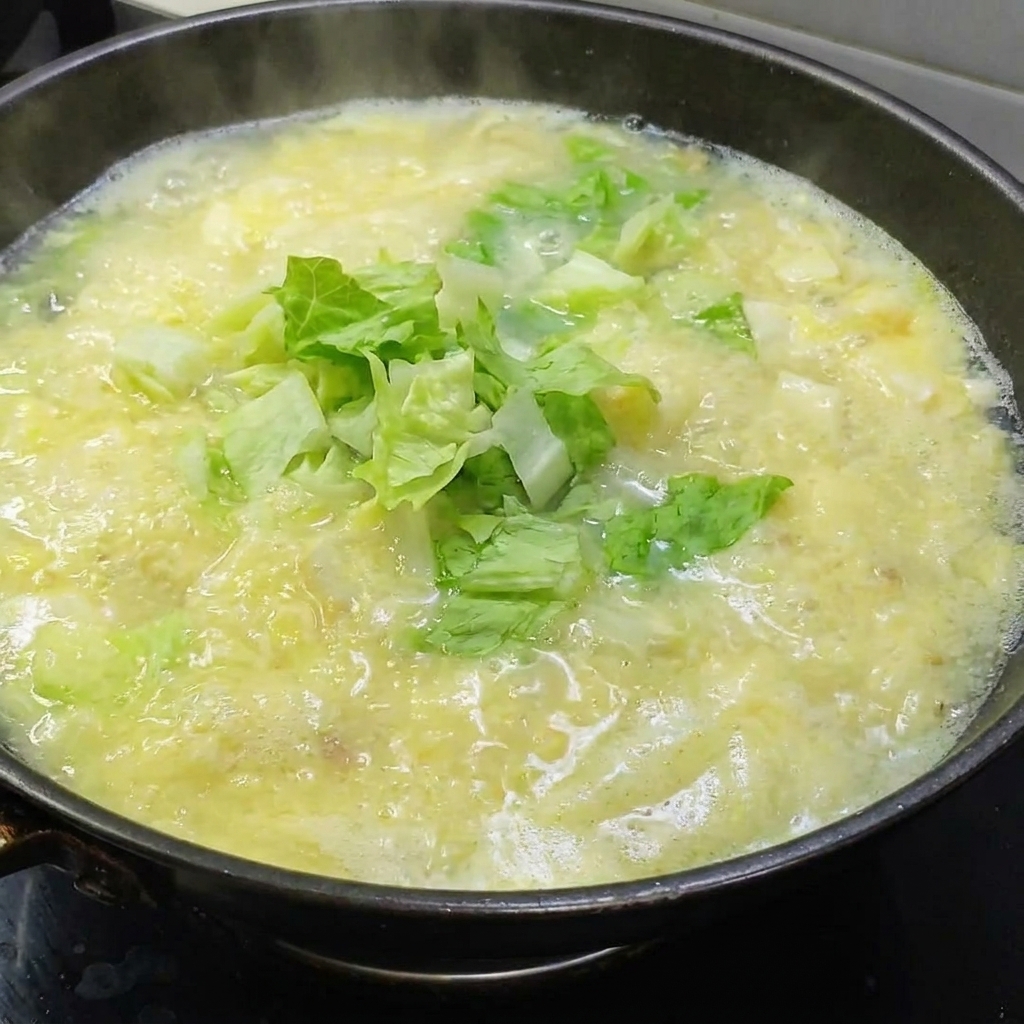 Foglie di lattuga verde fresca aggiunte a una pentola di zuppa dorata di tofu e uova salate.