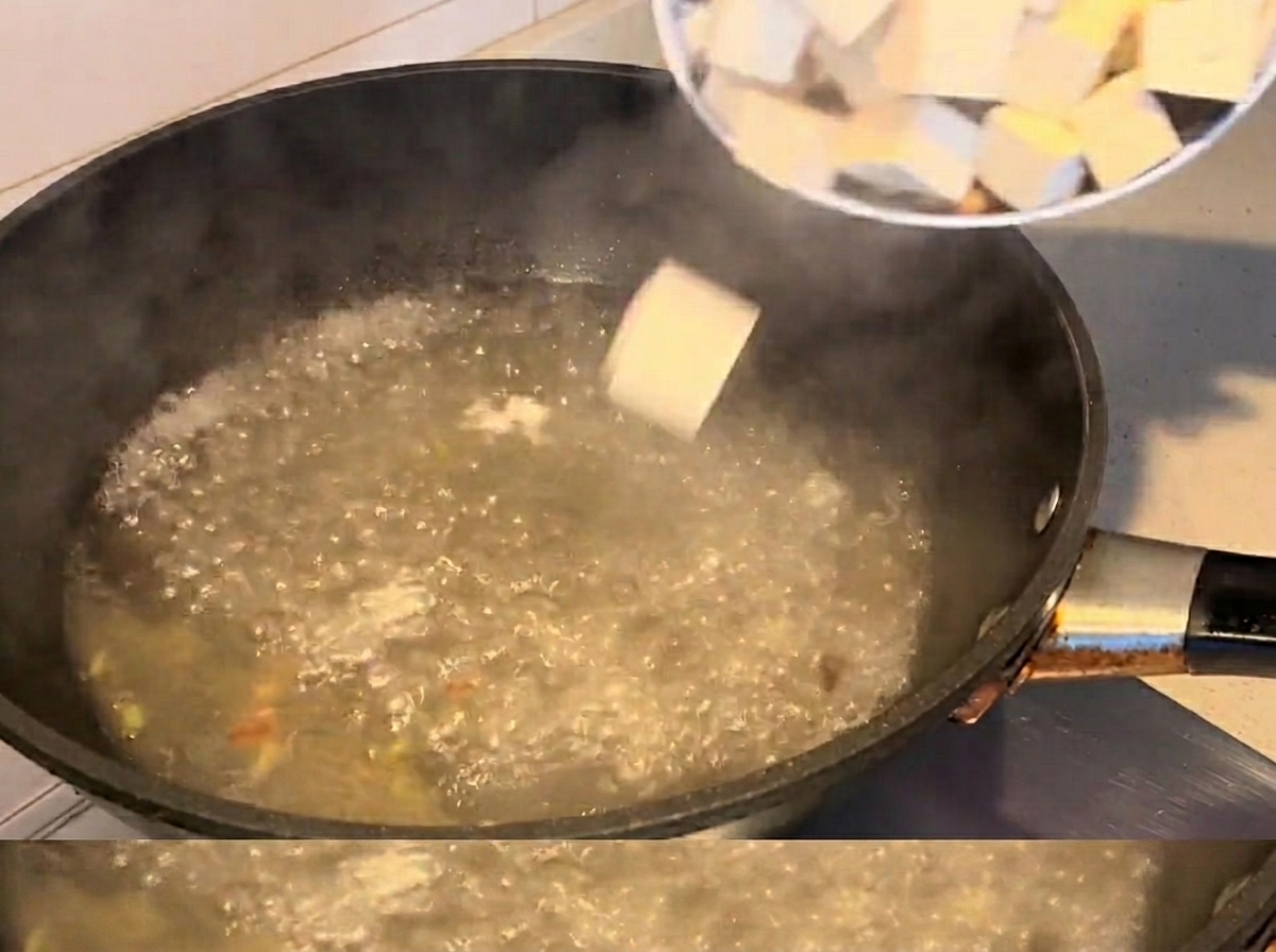 Cubetti di tofu e vongole che cuociono nella zuppa bollente.