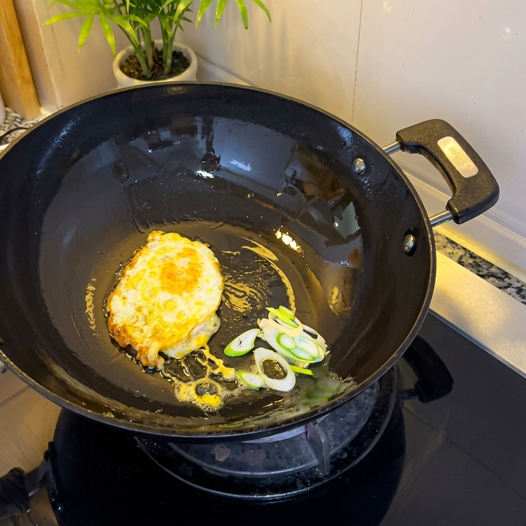 Uovo fritto e cipollotti tritati che sfrigolano nel wok.