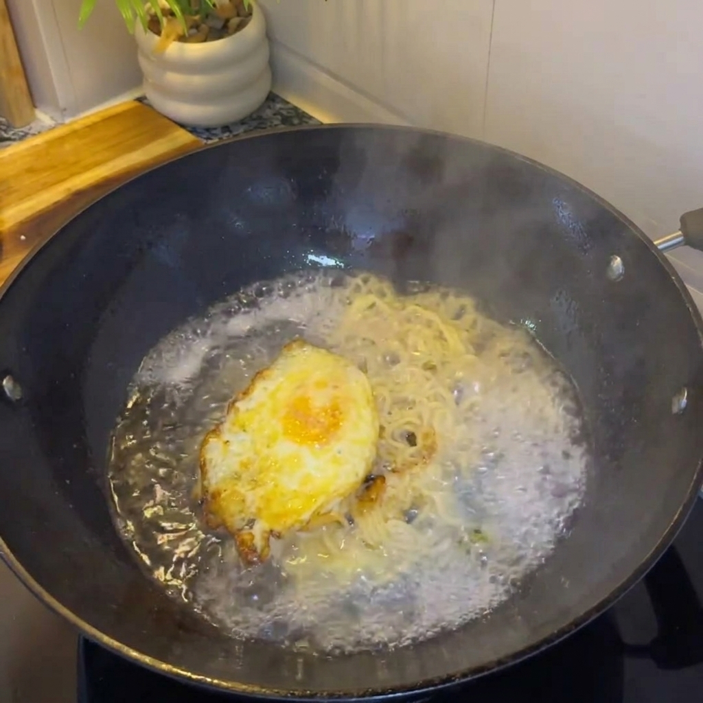 Acqua calda versata nel wok con luovo e i cipollotti per creare il brodo.