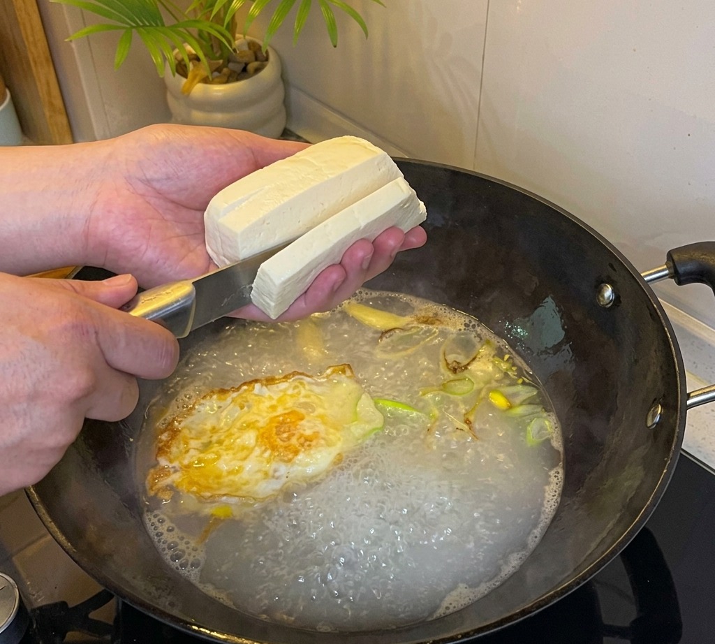 Tofu tagliato a cubetti aggiunto nel brodo bollente.