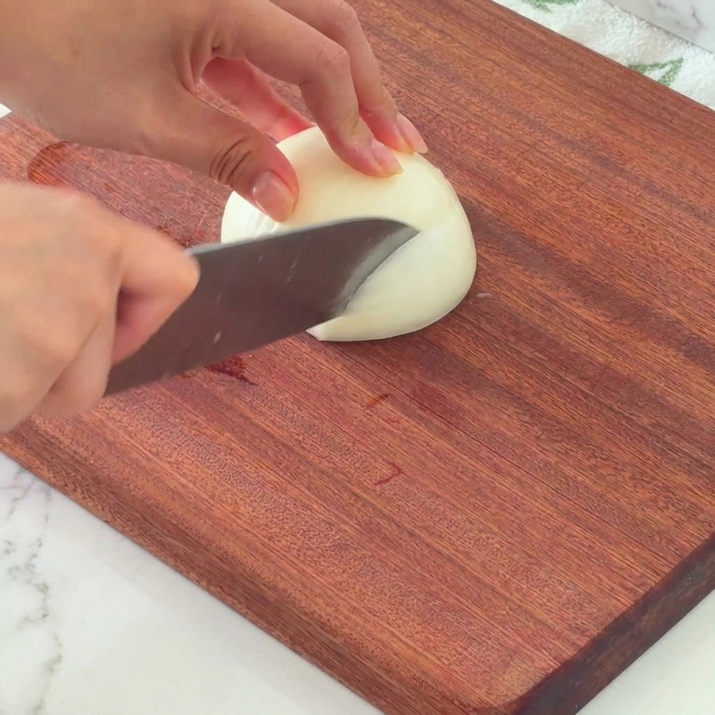 Metà di una cipolla bianca tagliata a dadini su un tagliere di legno.