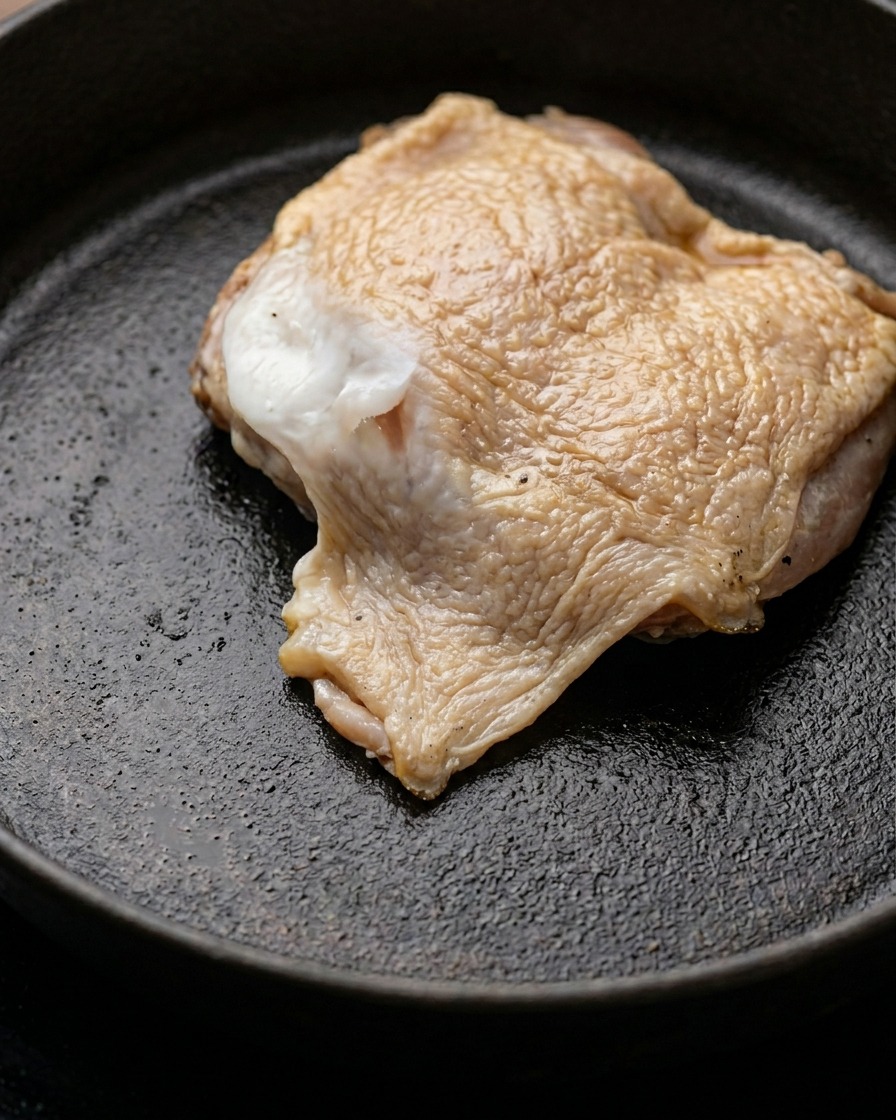 Un pezzo di sovracoscia di pollo marinata che rosola in una padella con burro fuso.