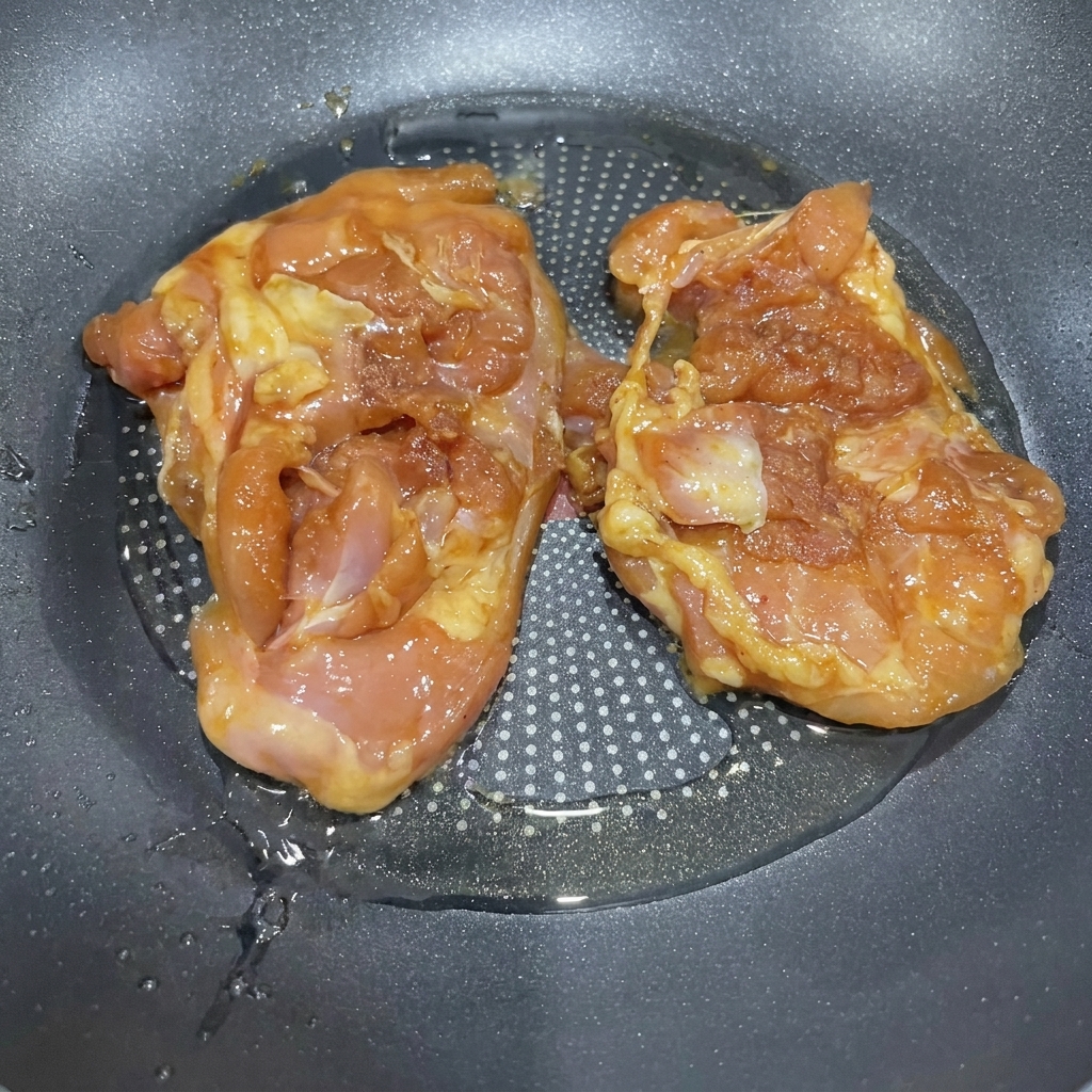 Cosce di pollo marinate che sfrigolano in padella con olio caldo.