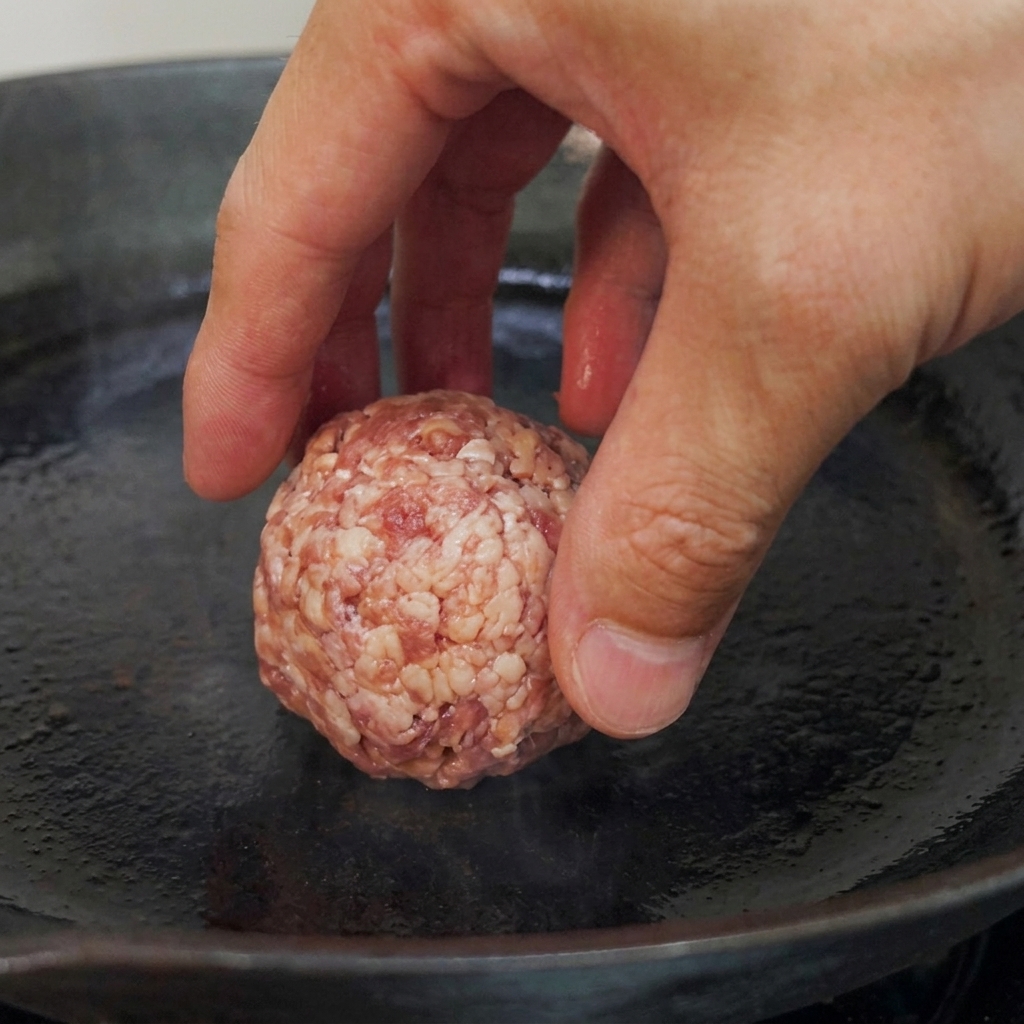 Polpette di carne cruda posizionate in una padella a fondo piatto preriscaldata, pronte per essere scottate.