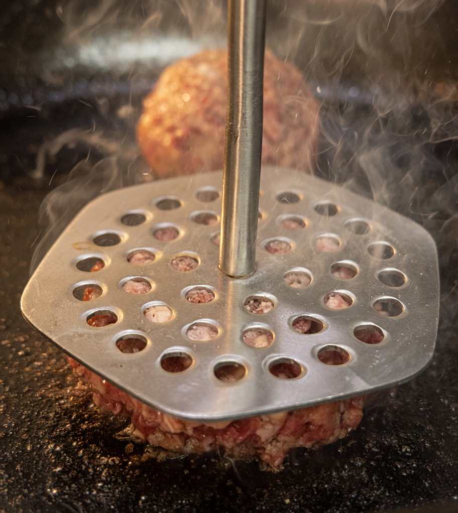 Una pressa per carne in metallo usata per schiacciare le polpette di manzo in hamburger sottili allinterno di una padella calda.