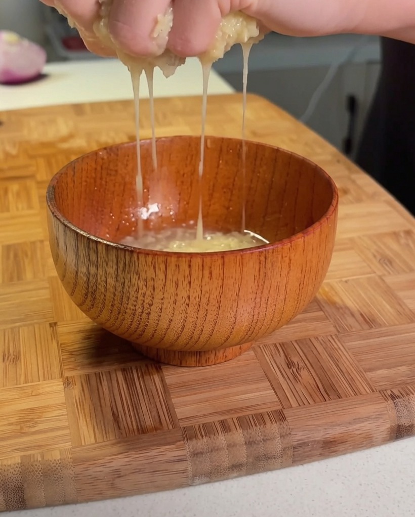 Mani che strizzano la patata grattugiata sopra una piccola ciotola di legno per estrarre il liquido.