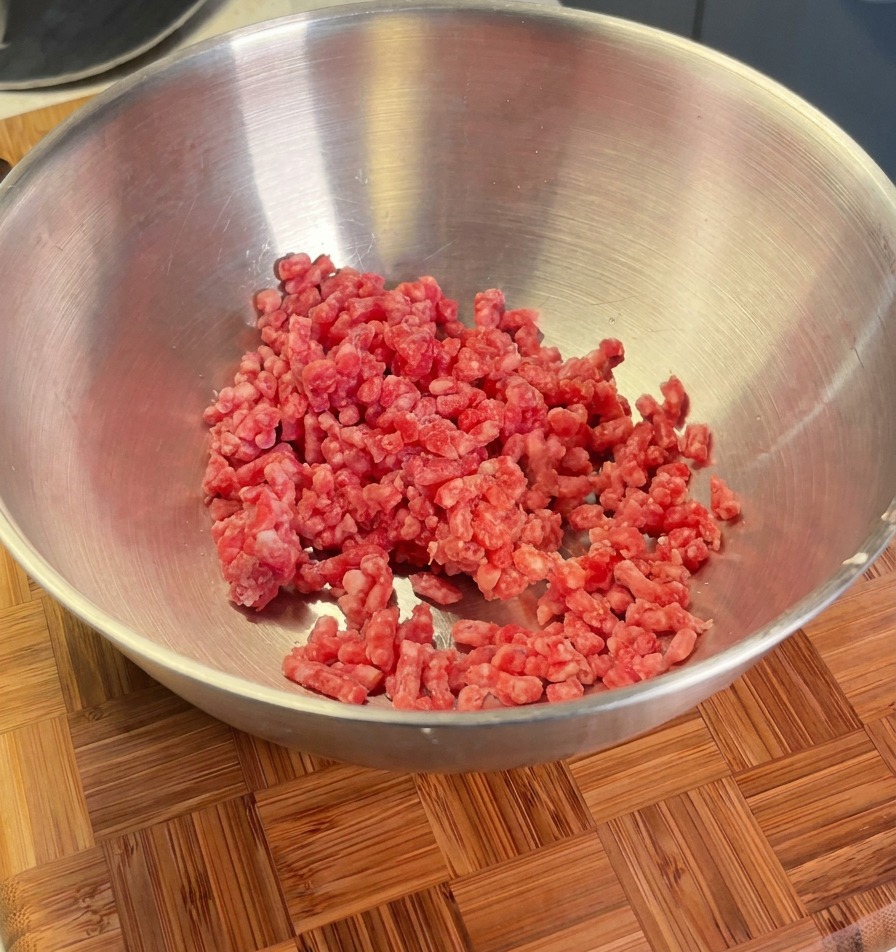Macinato di manzo in una ciotola di metallo pronto per essere condito con scalogni, sale e pepe nero.
