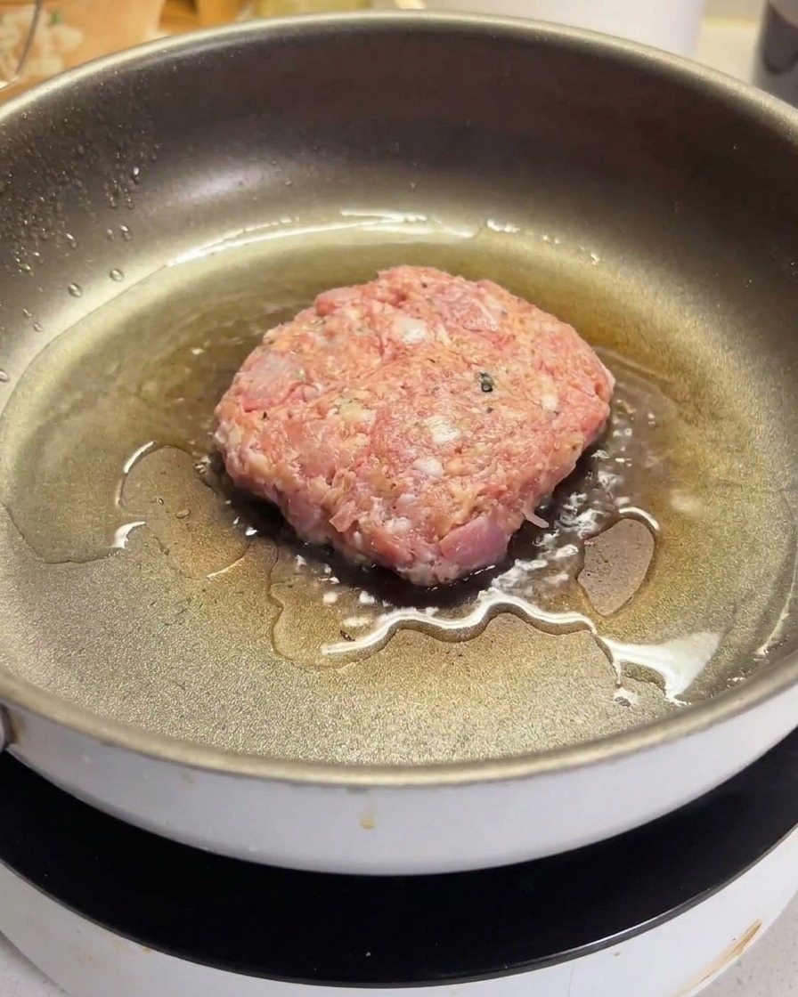 Un hamburger di manzo crudo che frigge in una padella antiaderente calda e oleata.