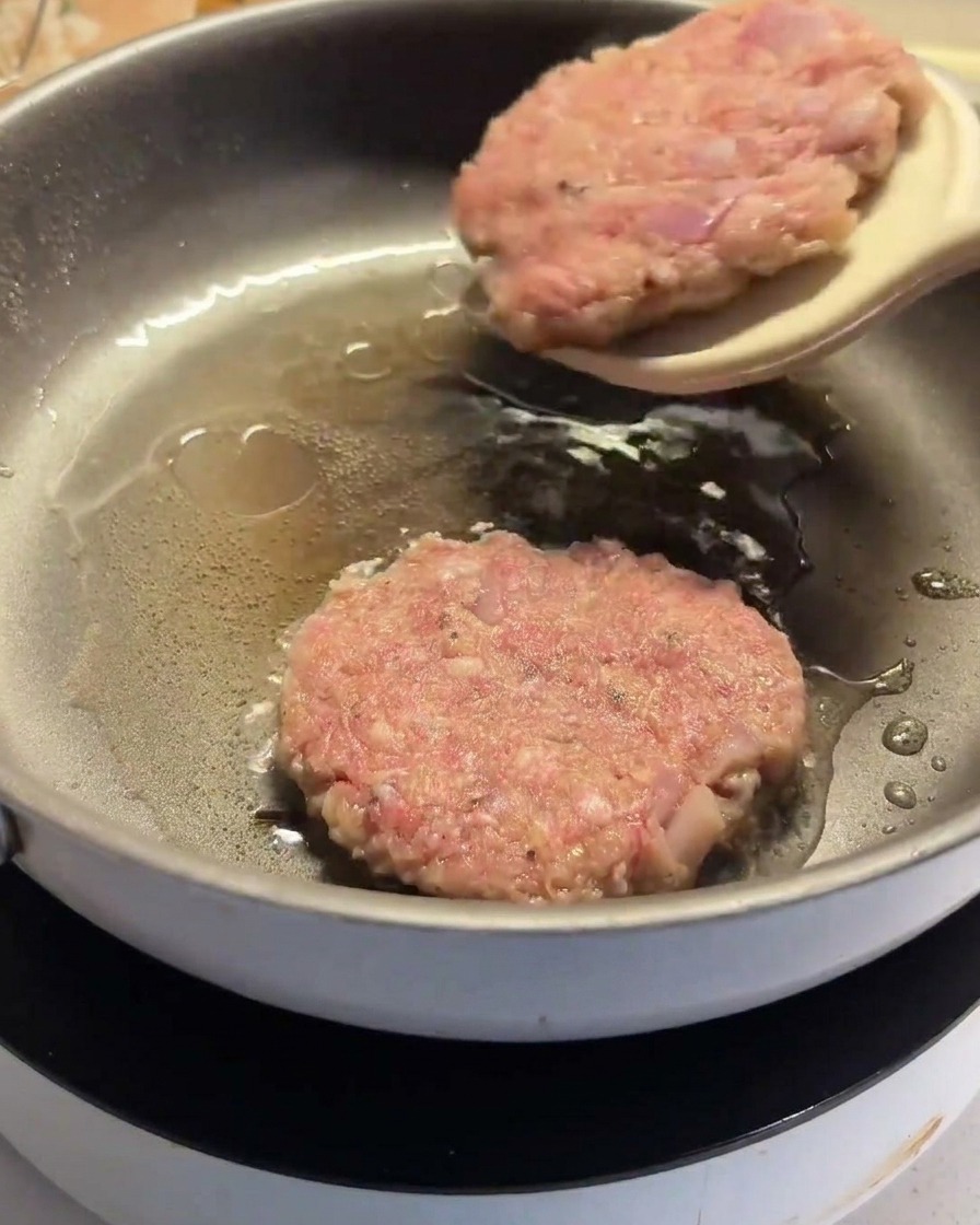 Una spatola che gira un hamburger parzialmente cotto nella padella.