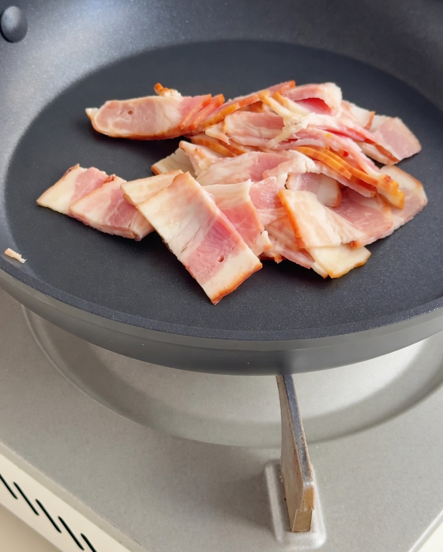 Pezzi di bacon in padella mentre diventano dorati e croccanti.