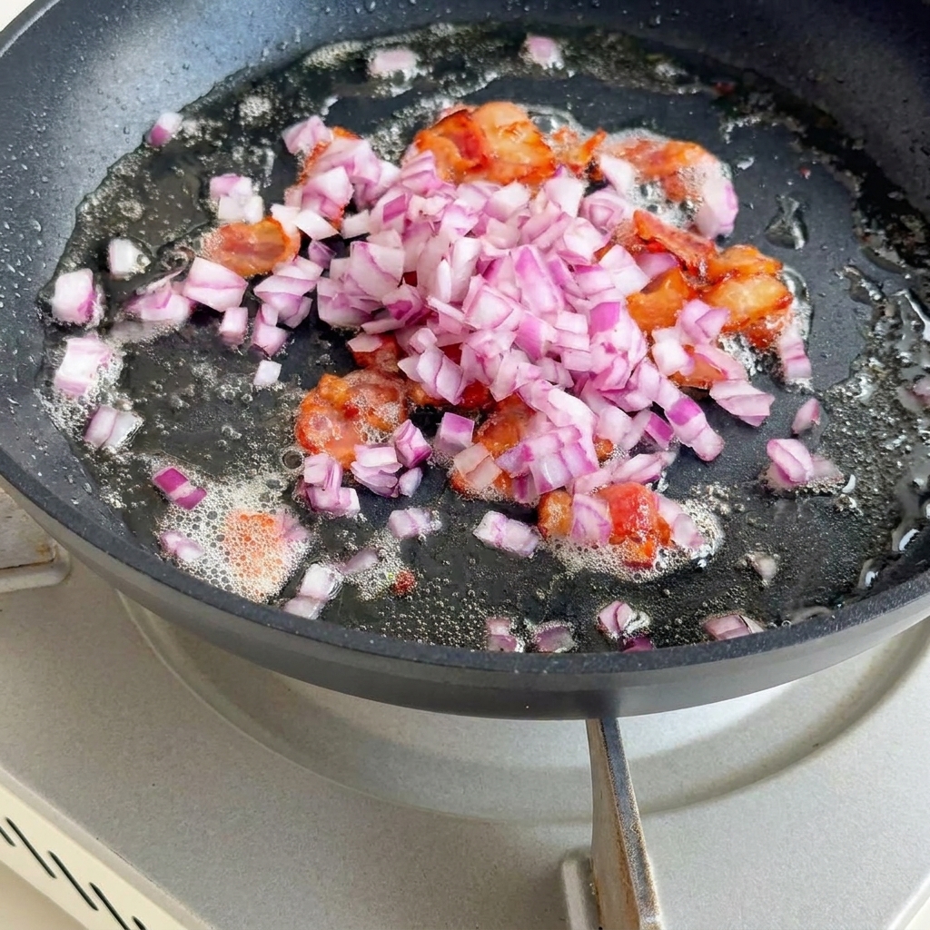 Cipolla, sedano e cubetti di patate che soffriggono con il bacon.