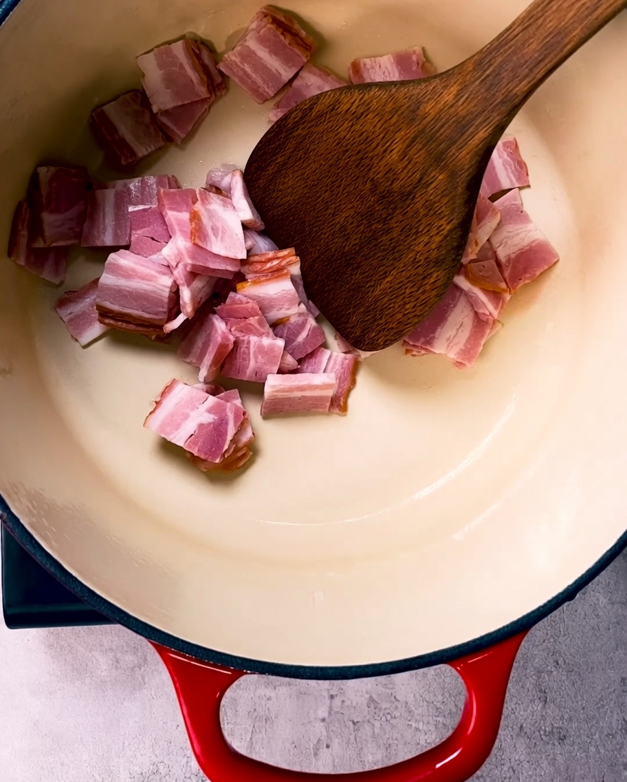 Pezzetti di pancetta dorati che friggono in una grande pentola di ghisa smaltata.