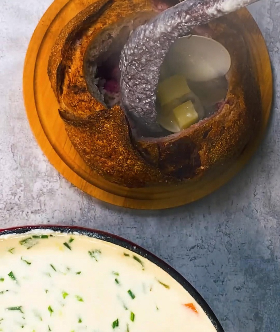 Zuppa di vongole cremosa versata in una ciotola di pane rustica, guarnita con pancetta croccante.