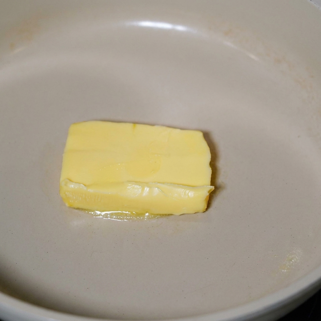 Bacon che frigge nel burro fuso in una padella.