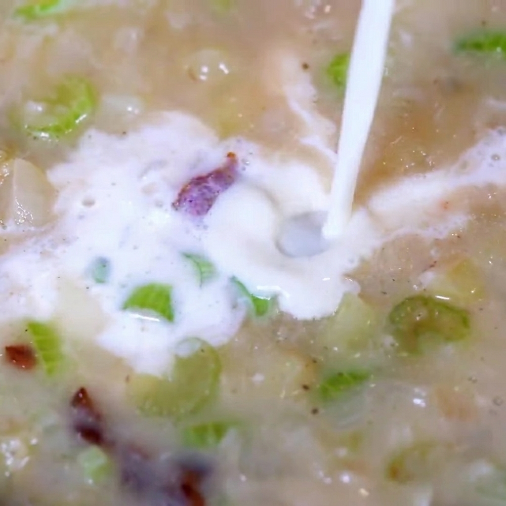Aggiunta della polpa di vongole tritata nella zuppa cremosa che sobbolle.