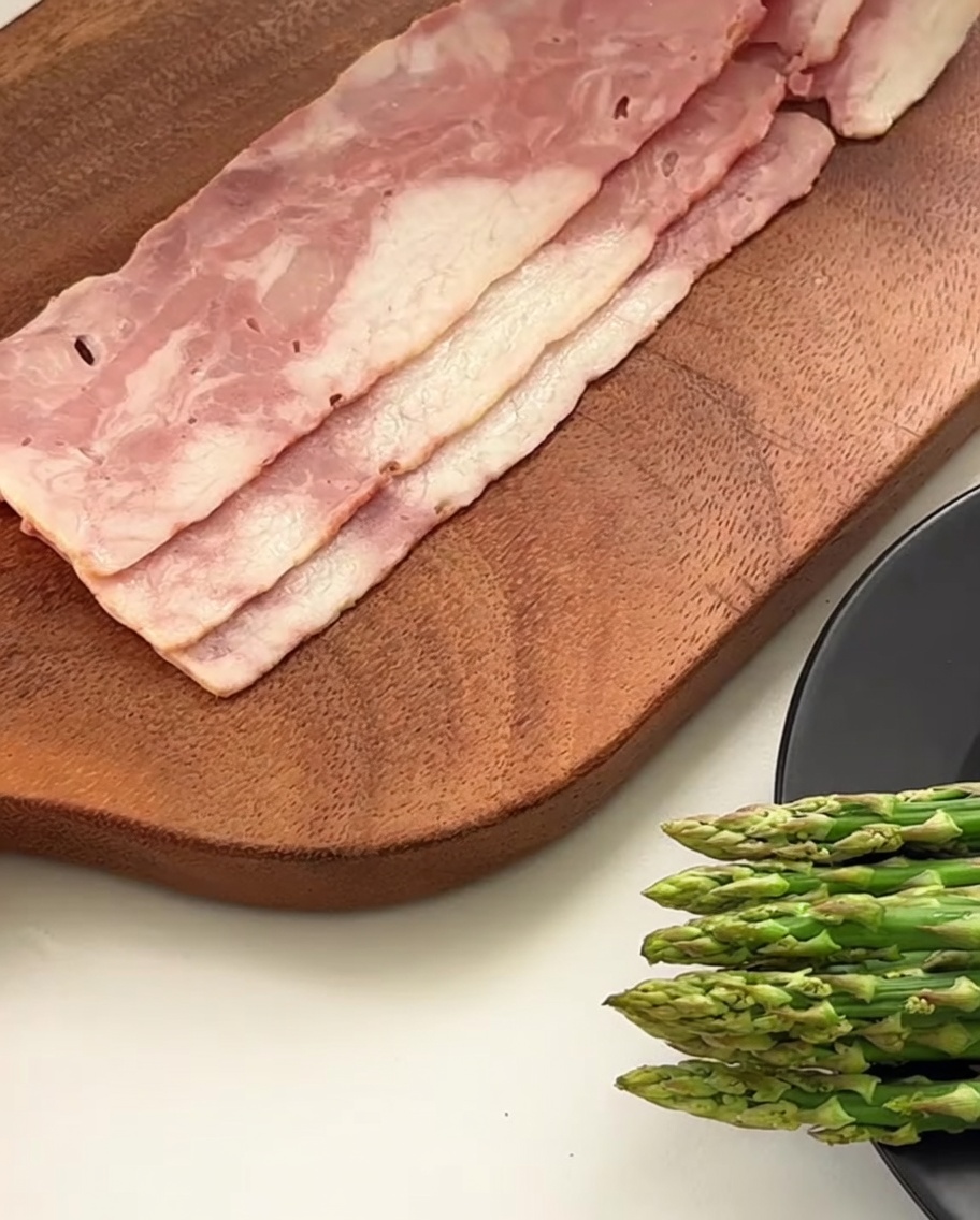 Primo piano di un coltello che taglia fette di pancetta in pezzi più piccoli su un tagliere di legno.