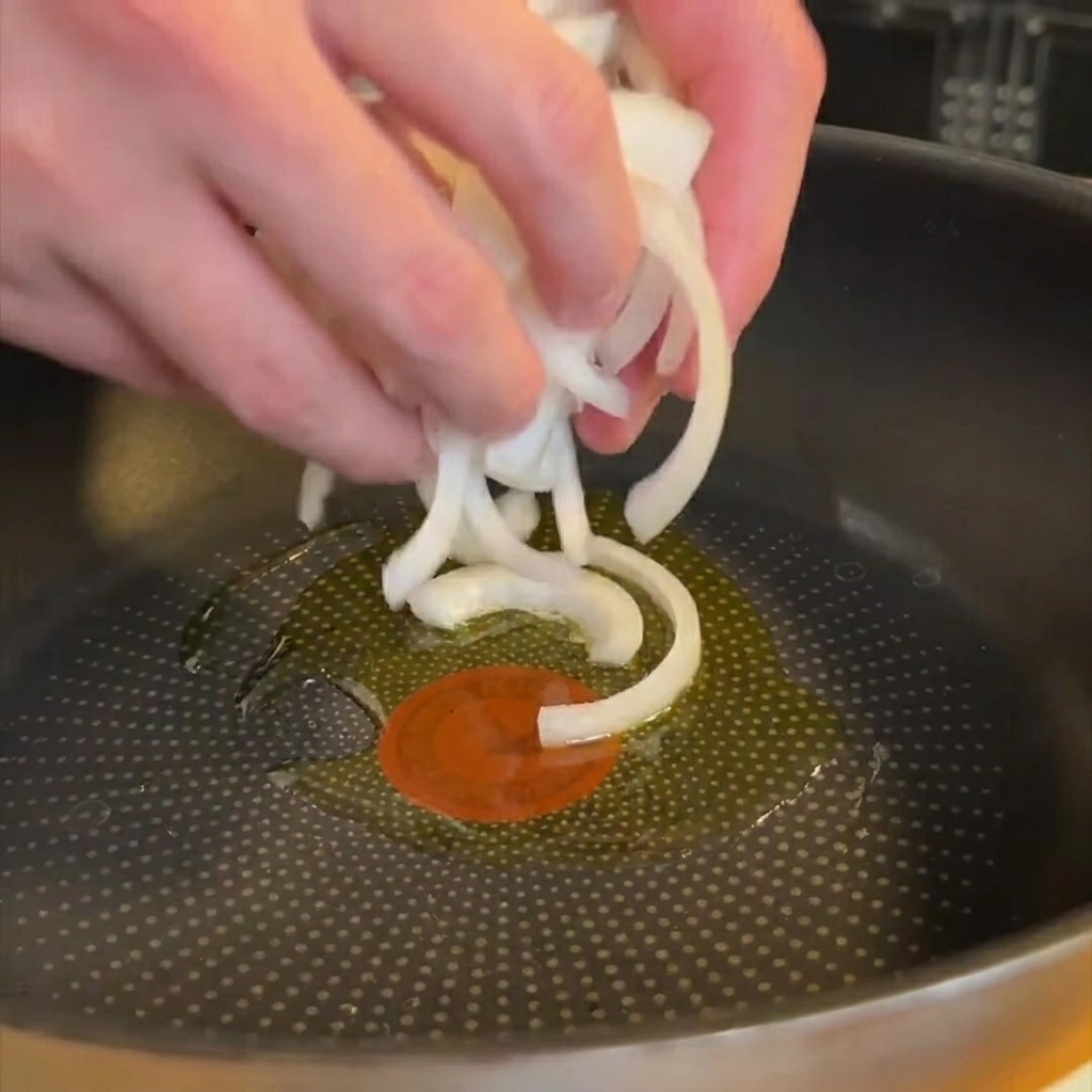 Cipolla affettata che appassisce in una padella con un filo dolio.