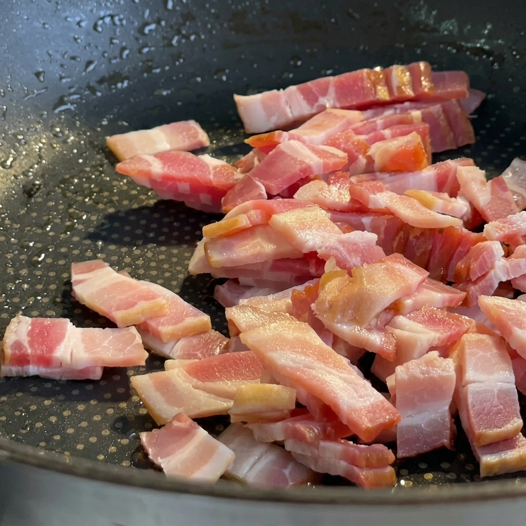 Pezzetti di pancetta che friggono in padella fino a diventare dorati e croccanti.