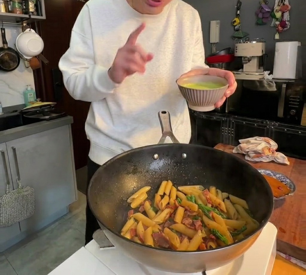 La crema verde di asparagi versata sulla pasta in padella e mescolata.