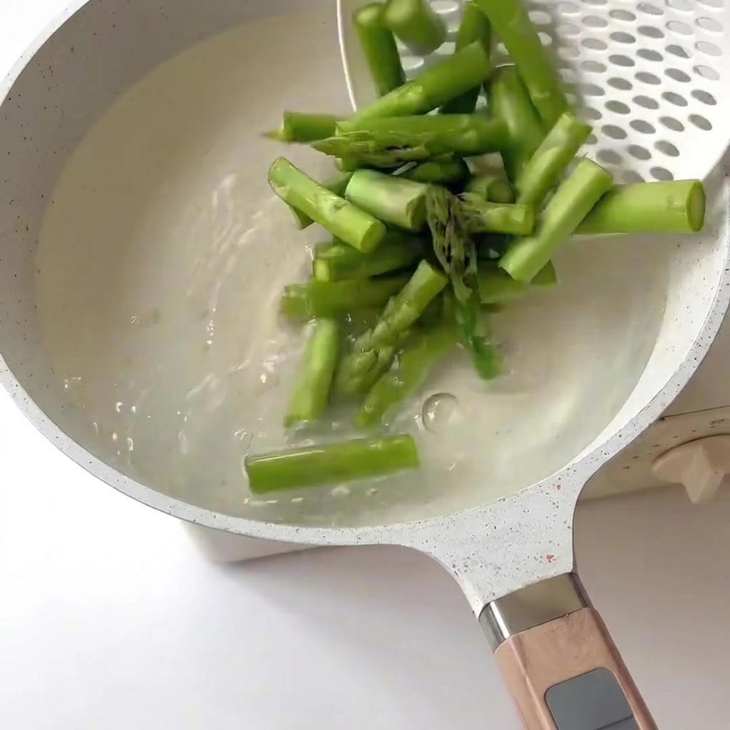 Pezzi di asparagi sbollentati in acqua bollente usando una schiumarola.