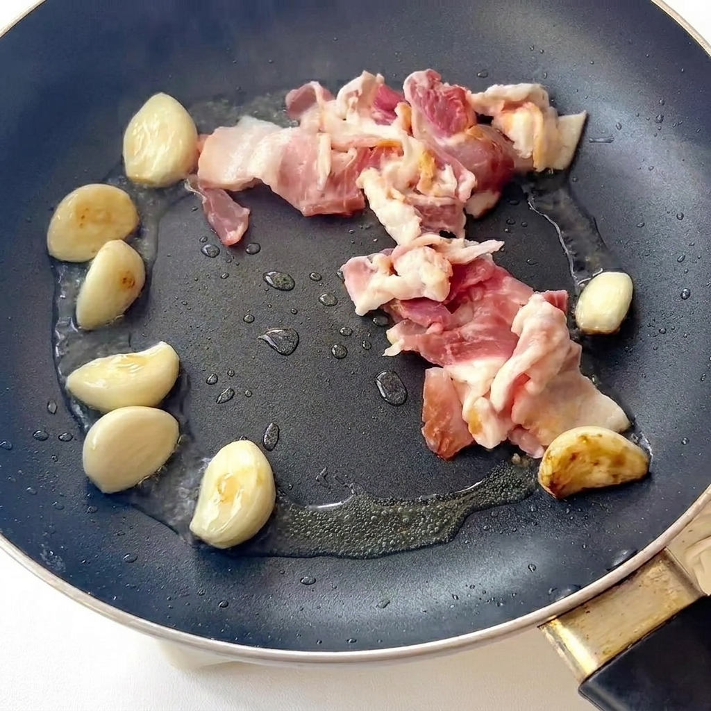 Pancetta che frigge in padella accanto agli spicchi daglio dorati.