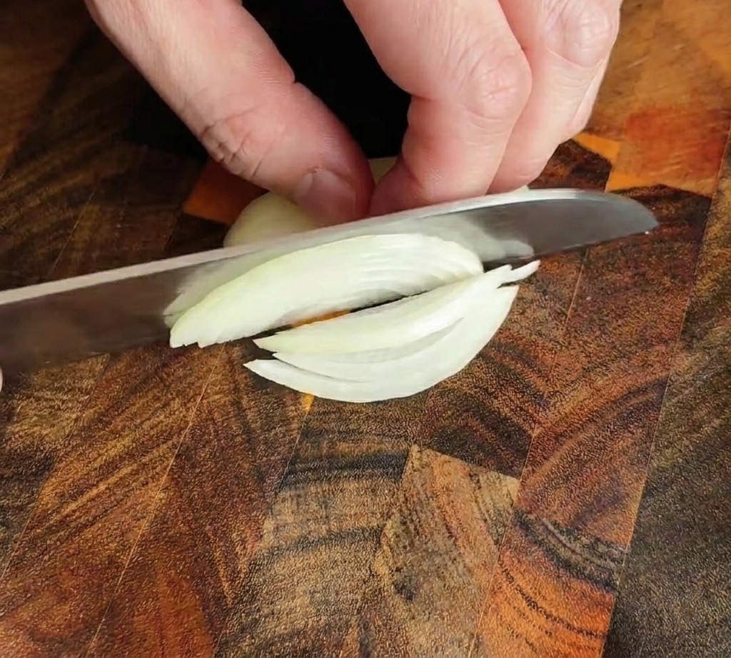 Un coltello da chef che affetta una cipolla a strisce sottili su un tagliere.