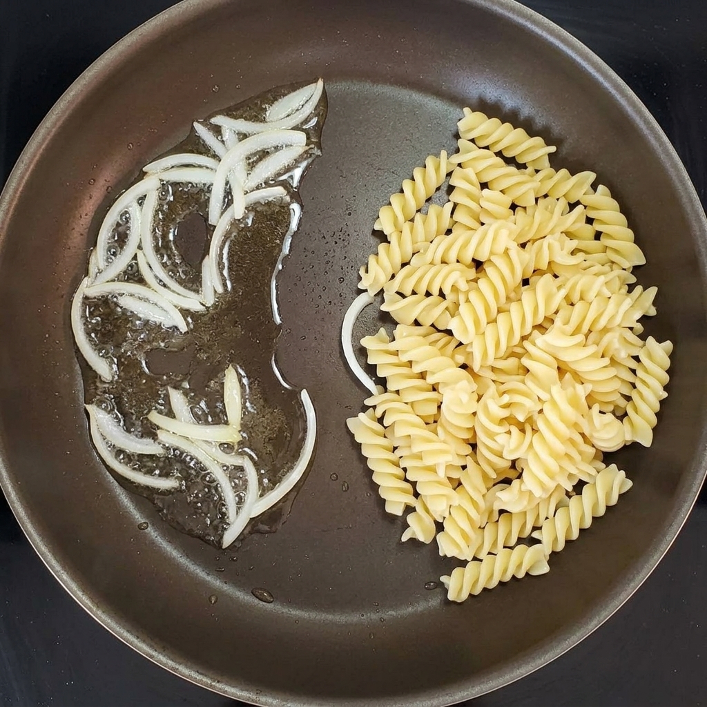 Pasta corta unita alle cipolle saltate in una padella.